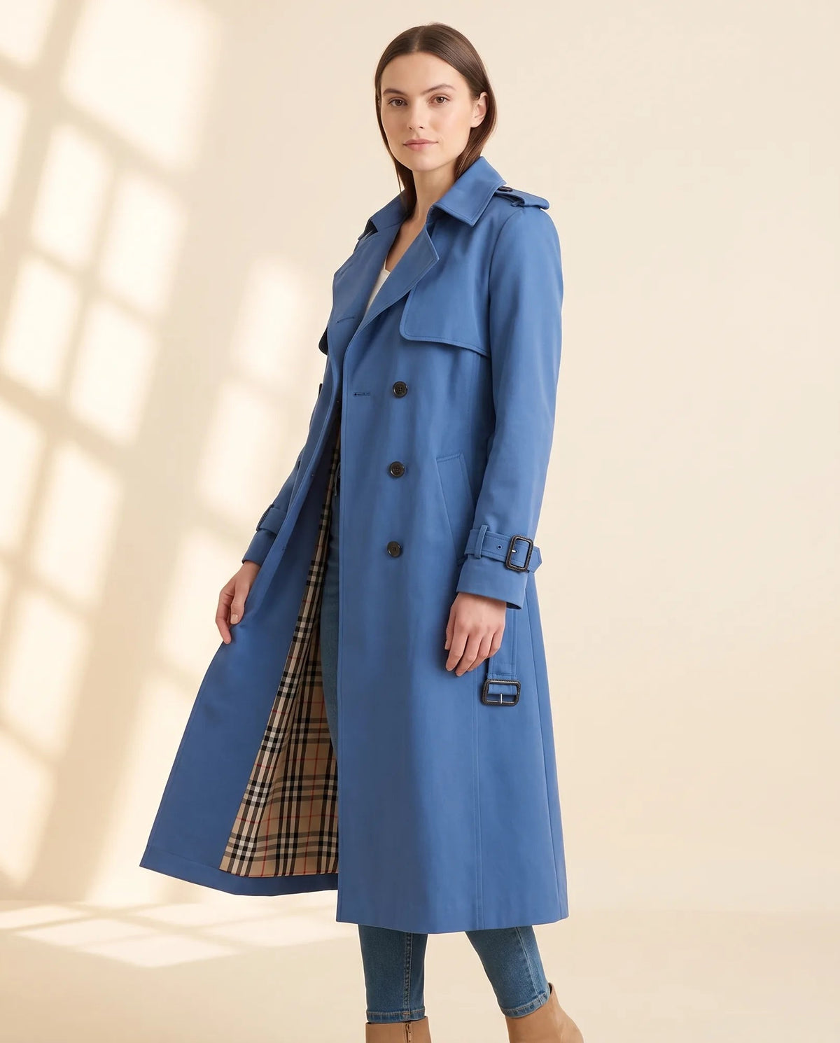 Angled view of blue longline trench coat worn open, showing check lining and cuff straps