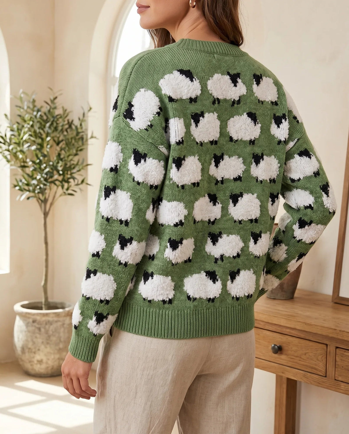 Back view of green knit sweater with fluffy white sheep motifs and ribbed hem