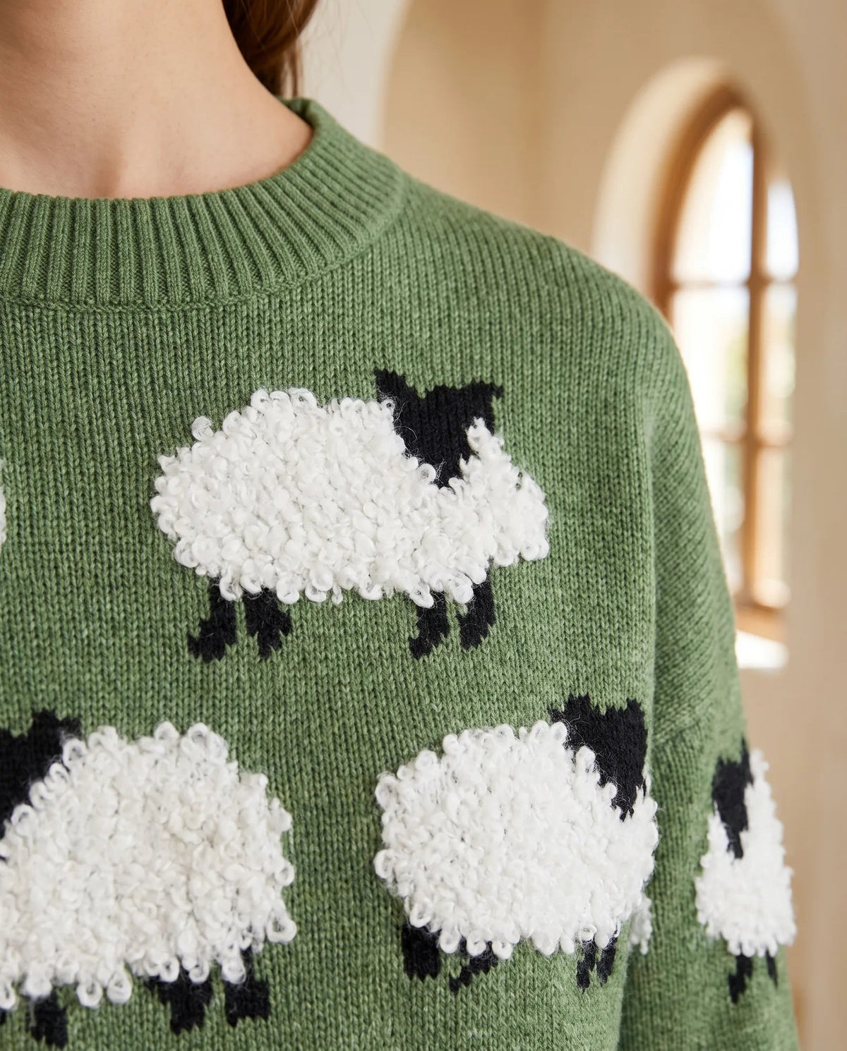 Close-up of raised white boucle sheep motif and ribbed green crew neckline
