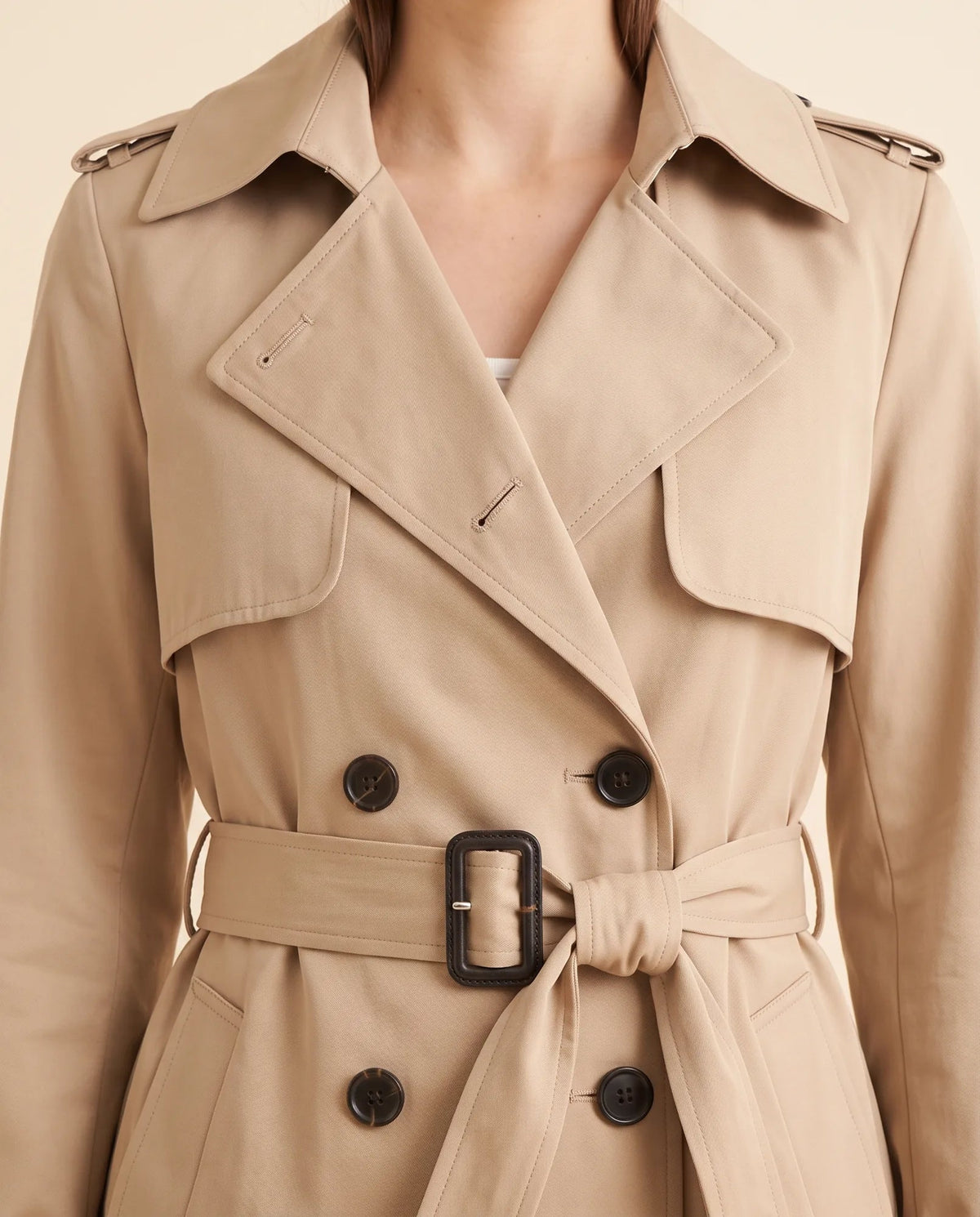 Close-up of beige trench coat showing notched lapels, double-breasted buttons and waist belt